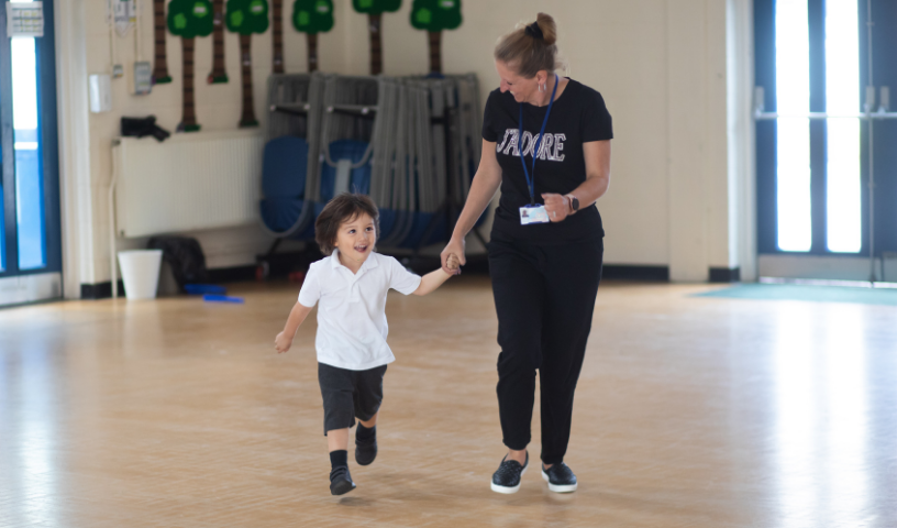 Practitioner and pupil running through sports hall, holding hands