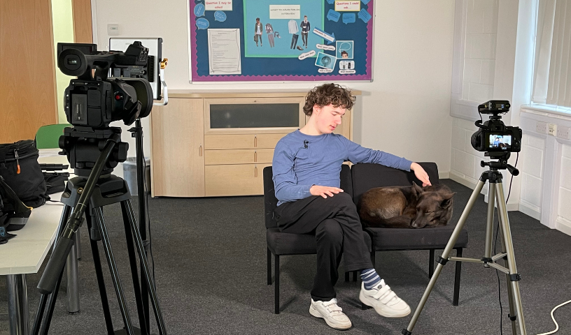 Post 16 learner sitting in front of camera, stroking a dog on the seat next to them