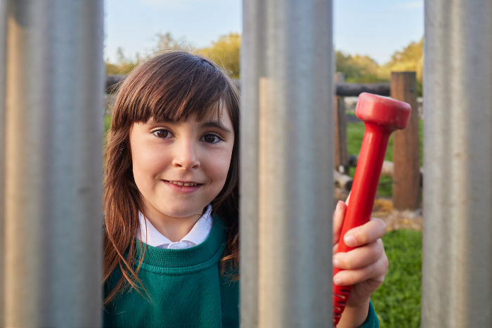 Child in school uniform, smiling at camera through school railings
