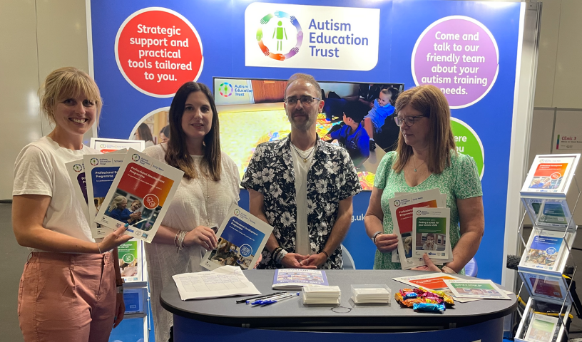 4 people who are Autism Education Trust staff and Partners, holding AET brochures and smiling at the camera on the AET Stand at The Autism Show