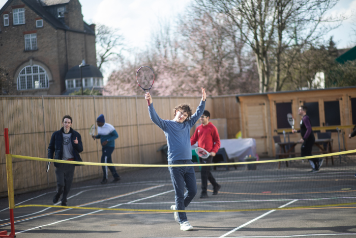 Young person standing on tennis court, both hands in their air.