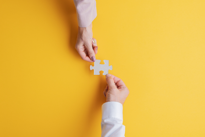 Two hands reach over a table and pass each other a puzzle piece