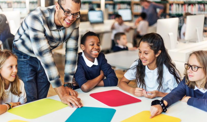 Teacher with school students at table with different coloured paper