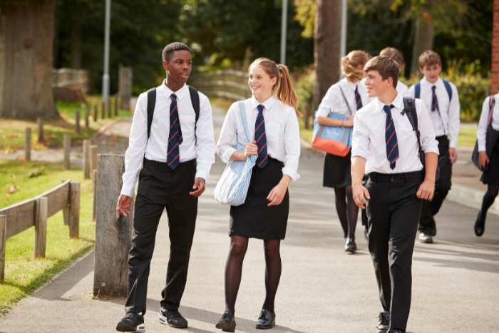 Three secondary pupils in shirts and ties, walking outside on school grounds, talking and smiling. 