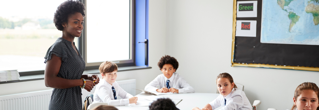 Teacher stands in classroom, a group of pupils sitting at their desks around them.