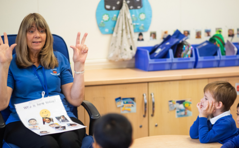 Practitioner in classroom. Holding up fingers as a classroom of children.