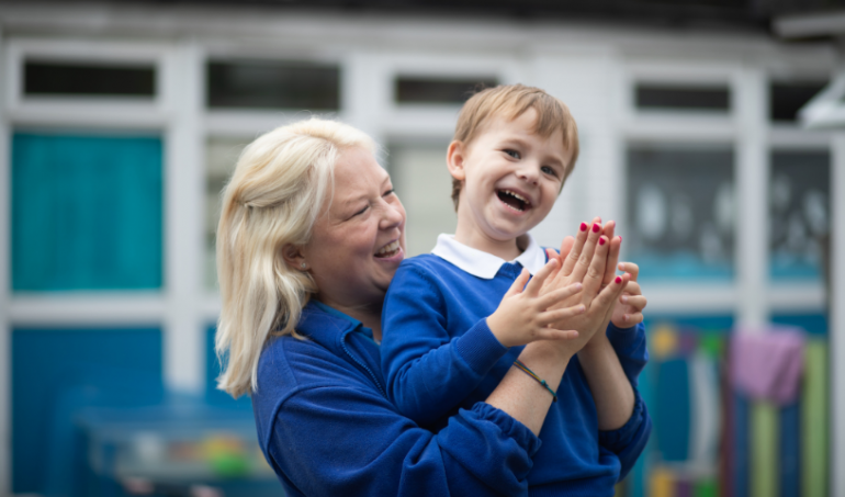 Practitioner and early years child clapping together