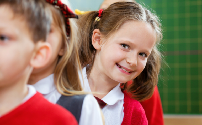 Primary pupil stood in line, leaning out and smiling at camera