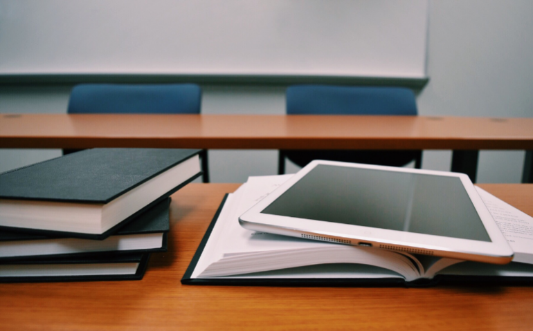 Pile of books on desk with computer tablet on top