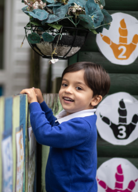 Early years child pulling self up toward top of wall, smiling.