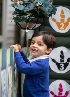 Early years child pulling self up toward top of wall, smiling. 