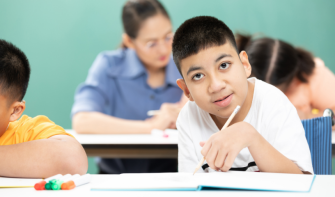 Pupil holding pencil over paper and looking up at the camera