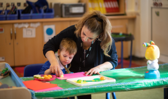 Child doing crafts in classroom with practitioner 