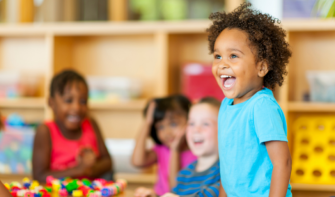 Child stood up at table in classroom, smiling