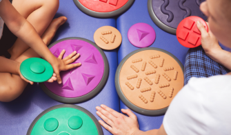 Birds eye view photo of two people touching colourful, textured, sensory disks