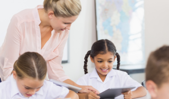 Teacher helping primary school pupil, smiling, looking at computer tablet