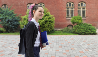 Post 16 learner with pink hair, walking outside school building, smiling, holding folder