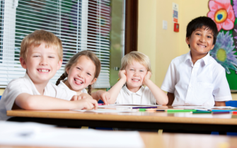 Primary school pupils smiling at camera, sat at desk in classroom