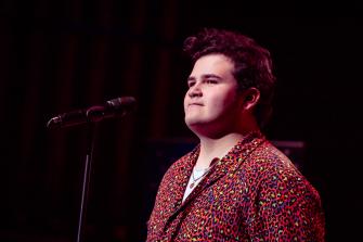 Performer standing on stage in front of a microphone. They are smiling. 