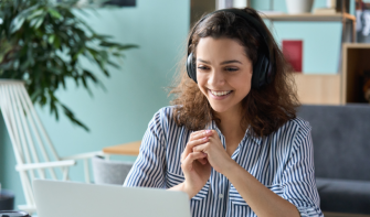 Person sits in front of a laptop with headphones on, smiling at the screen.