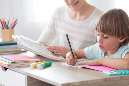Child sitting with adult, concentrating on drawing with pencil