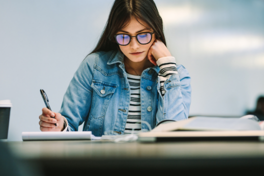 Young adult sitting at desk, looking at paper, pen in hand