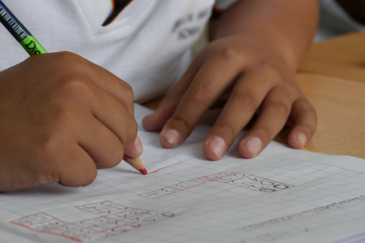 Child's hands writing at desk, wearing white polo top