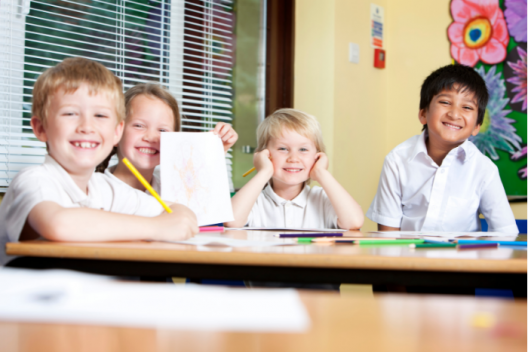 Group of students smiling at desk with paper and pencils in hand