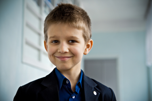 Primary school aged pupil in black blazer and blue shirt, smiling at camera