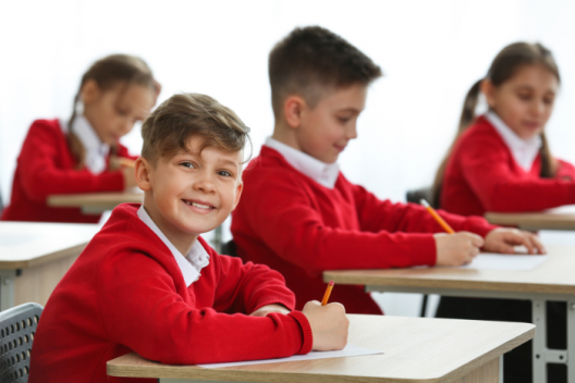 Pupils in exam room in red school uniform. One looking across room at camera, smiling. 