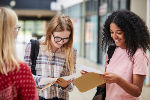 3 pupils opening results envelopes together, smiling at the papers they are holding