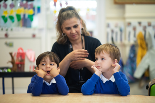 Primary school pupils in school uniform sitting with education practitioner, looking ahead