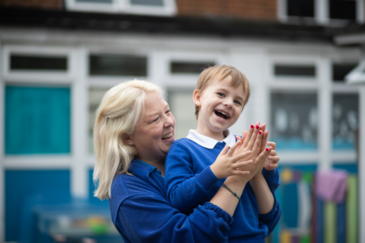 Early years child with practitioner, clapping hands and smiling