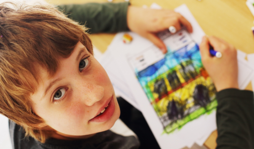 Boy in school uniform, drawing, looks up at camera