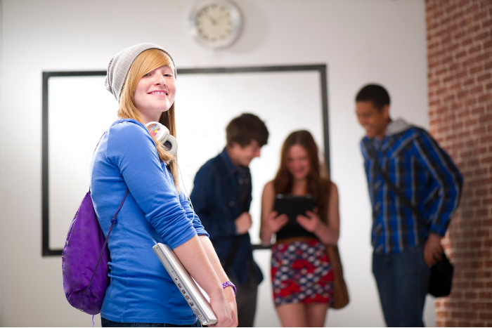 Sixth form student holding laptop, looking to the side at camera, smiling.