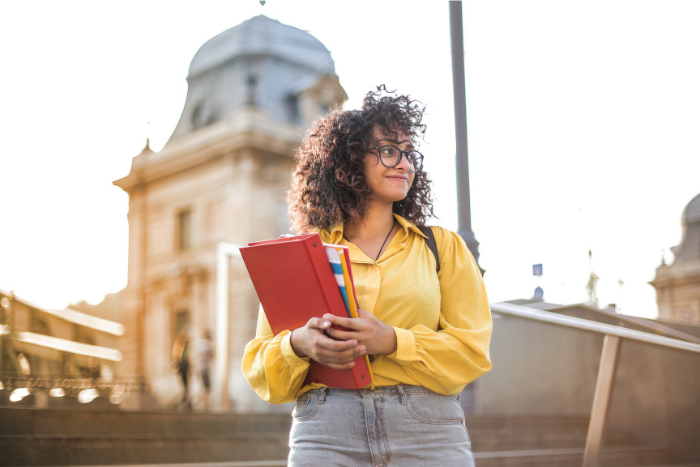 young pupil standing outside holding work books, looking around, smiling