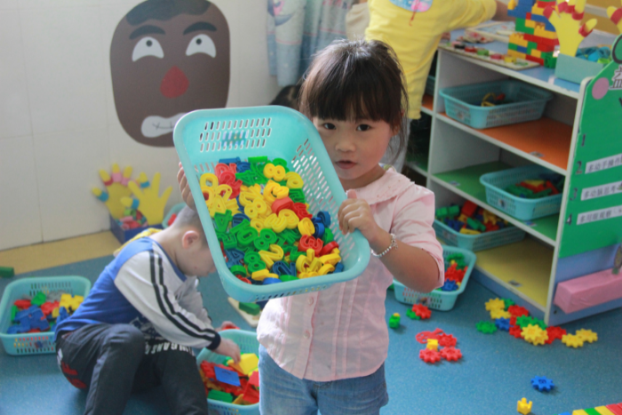 Child in nursery, holding up box of toys