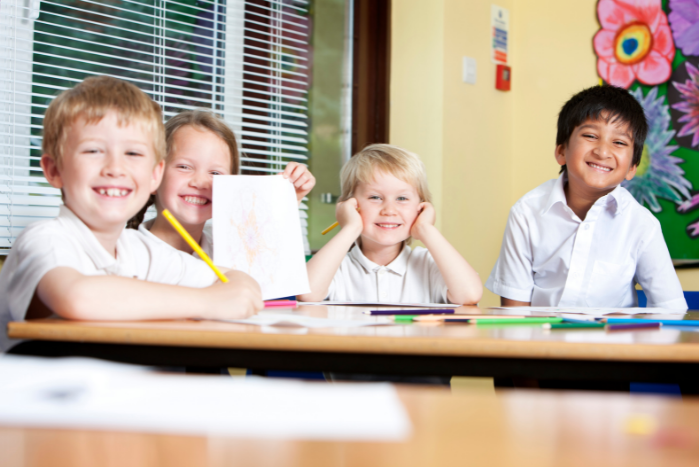 Group of students smiling at desk with paper and pencils in hand