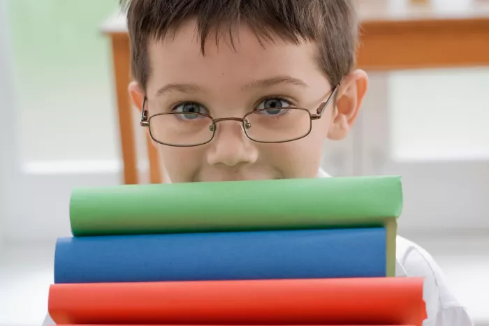 Child in glasses carrying stack of books, his face showing from the nose up. 