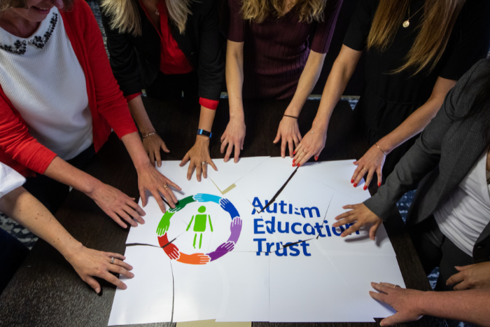 Autism Education Trust Logo printed on poster puzzle. Hand pushing the pieces together 