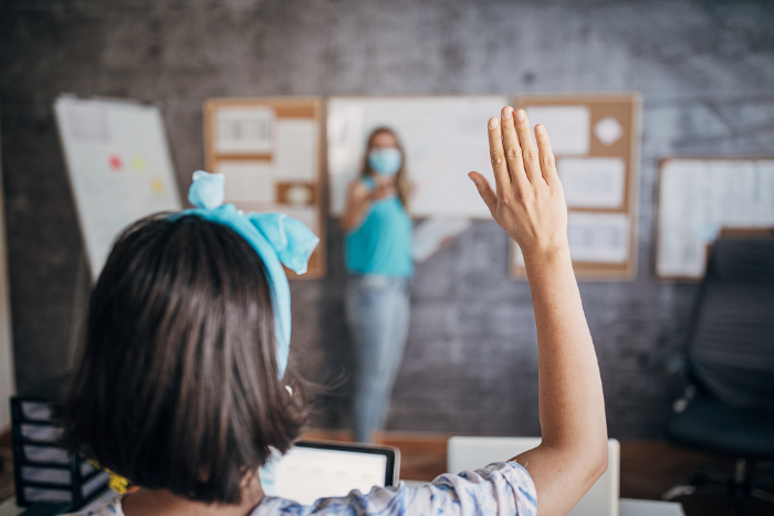 Pupil raising hand in classroom, looking ahead at teacher
