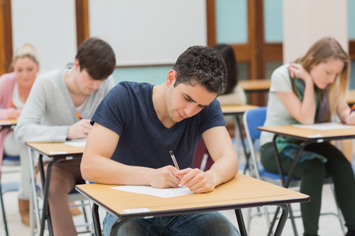 A level student sitting in exam room, working on exam paper.