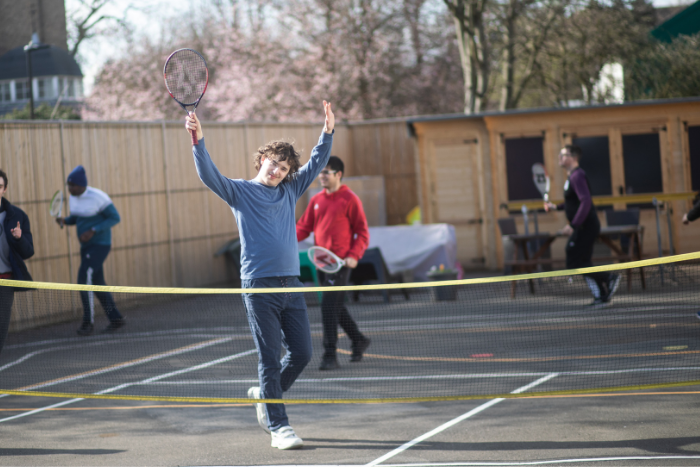 Young person on tennis court, holing up racket and arms, almost cheering