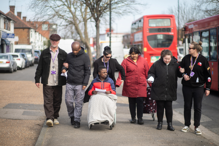 Group of young autistic people and practitioners, walking down street, linking arms