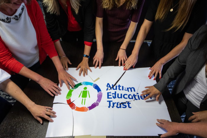 A number of hands pushing together a paper puzzle AET logo